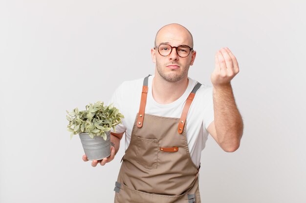 Homem jardineiro fazendo gesto capice ou dinheiro, dizendo para você pagar suas dívidas!