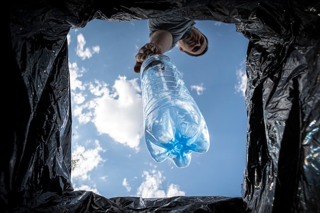 Homem joga a garrafa de plástico vazia em uma lata de lixo. Vista inferior da lata de lixo. O problema da reciclagem e poluição do planeta com lixo.