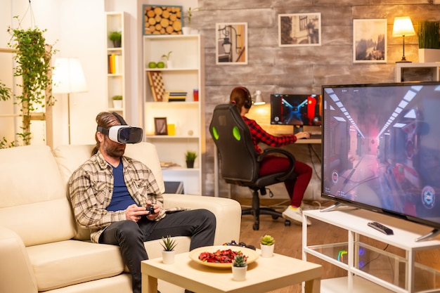 Homem-jogador usando um fone de ouvido de realidade virtual para jogar videogame na sala de estar tarde da noite