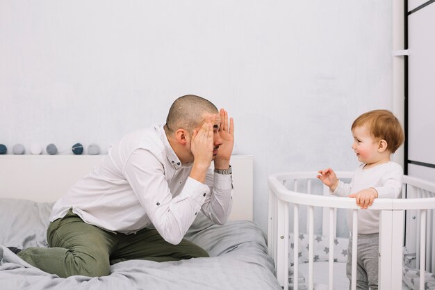 Foto homem jogando com sorrindo bebezinho no berço no quarto