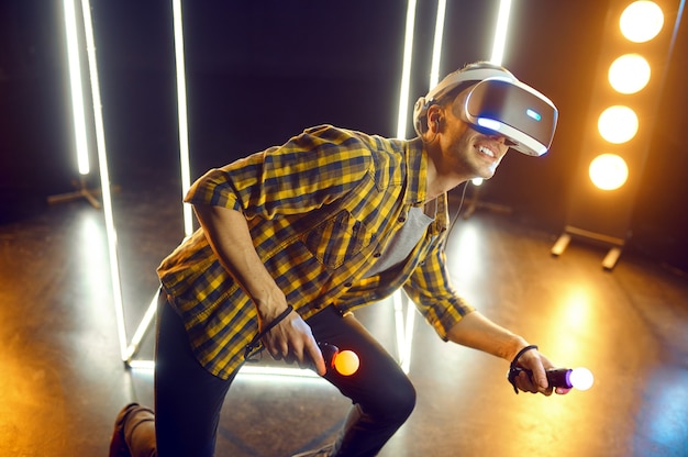 Homem jogando em fone de ouvido de realidade virtual e gamepad em cubo luminoso