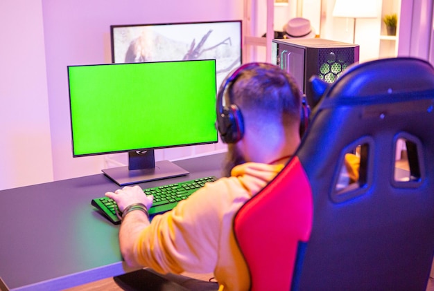 Foto homem jogando em um poderoso pc gaming em uma sala com luzes de néon em um computador de tela verde.