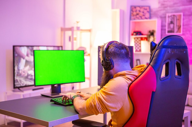 Homem jogando em um poderoso pc gaming em uma sala com luzes de néon em um computador de tela verde.