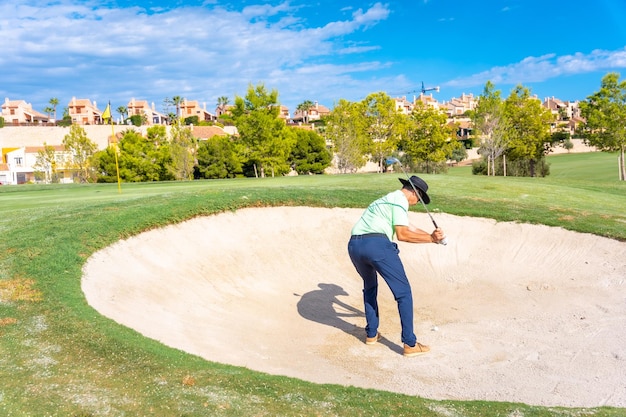 Homem jogando golfe no bunker batendo na bola com a cunha de arremesso de taco