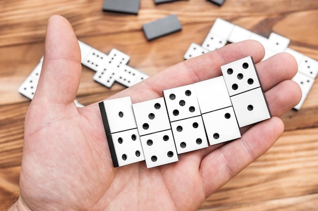 Homem jogando jogo de dominó Feche a mão segurando peças de dominó sobre a mesa com jogo de dominó