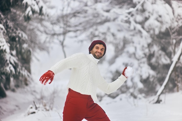 Homem jogando jogo de inverno jogando bola de neve em uma floresta montanhosa ao ar livre