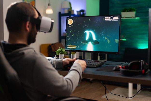 Homem jogando videogame com fone de ouvido vr no computador, usando equipamentos de jogos. Jogador com óculos de realidade virtual segurando joystick para jogar jogos online. Jogador usando o controle para o jogo