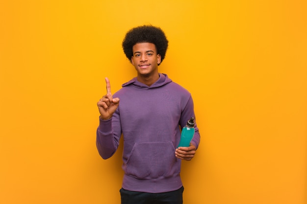 Homem jovem afro-americano fitness segurando uma bebida energética, mostrando o número um