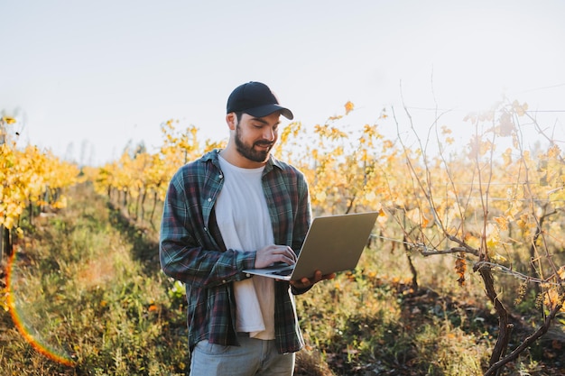 Homem jovem agricultor latino trabalhando em seu laptop no meio de sua plantação de vinha