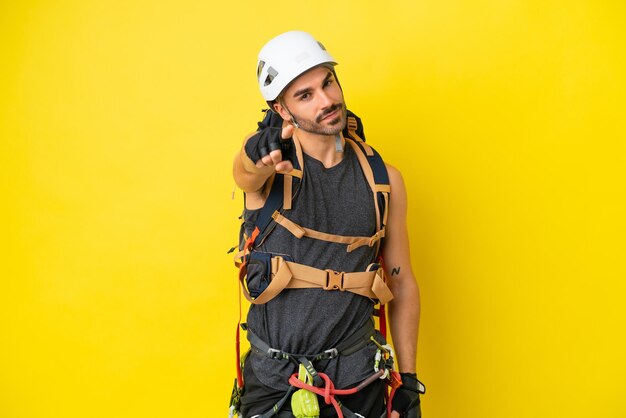 Homem jovem alpinista caucasiano isolado em fundo amarelo aponta o dedo para você com uma expressão confiante