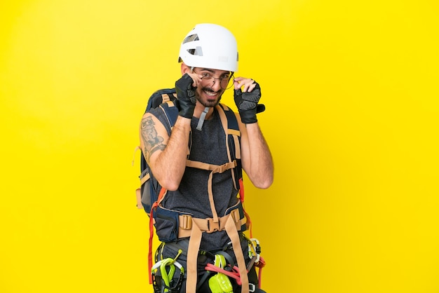 Homem jovem alpinista caucasiano isolado em fundo amarelo com óculos e surpreso