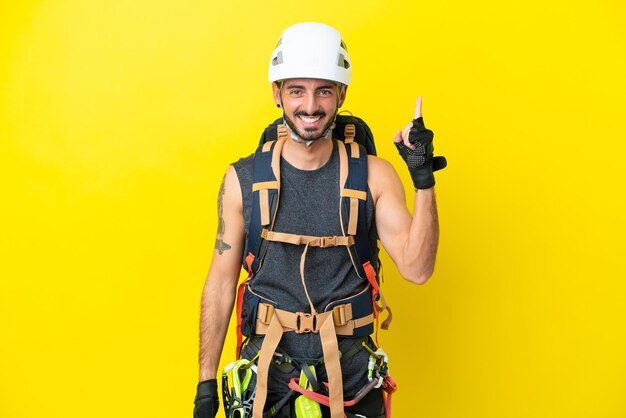 Homem jovem alpinista caucasiano isolado em fundo amarelo mostrando e levantando um dedo em sinal do melhor