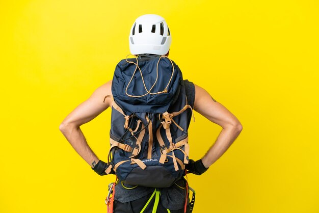 Homem jovem alpinista caucasiano isolado em fundo amarelo na posição traseira