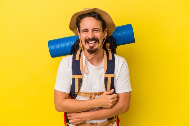 Homem jovem alpinista caucasiano isolado em fundo amarelo, rindo e se divertindo.