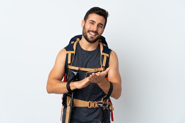 Homem jovem alpinista com uma mochila grande e pólos de trekking isolados na parede branca aplaudindo
