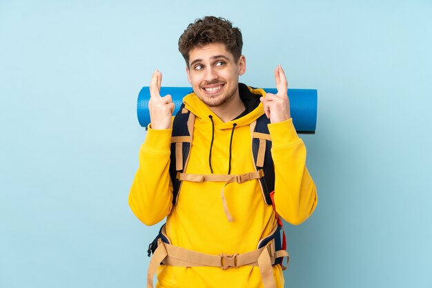 Homem jovem alpinista com uma mochila grande na parede azul com dedos cruzando