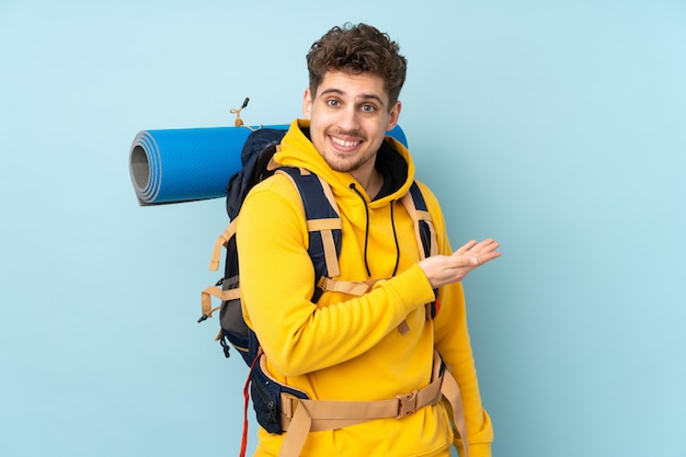 Homem jovem alpinista com uma mochila grande na parede azul, estendendo as mãos para o lado