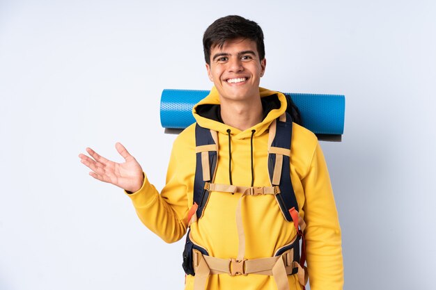Homem jovem alpinista com uma mochila grande sobre azul isolado segurando copyspace imaginário na palma da mão