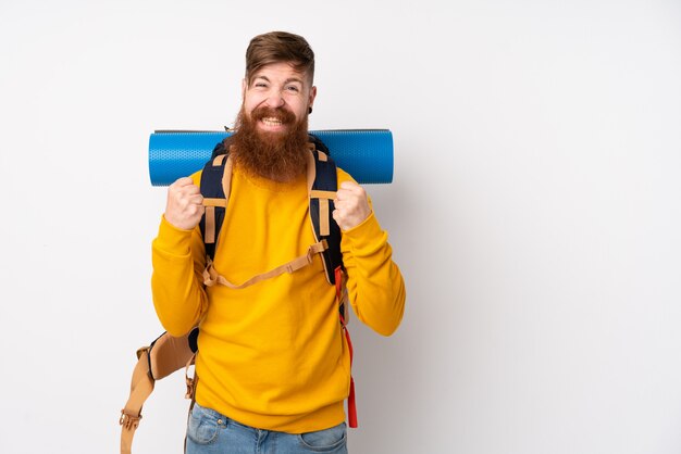 Homem jovem alpinista com uma mochila grande sobre parede branca isolada, comemorando uma vitória