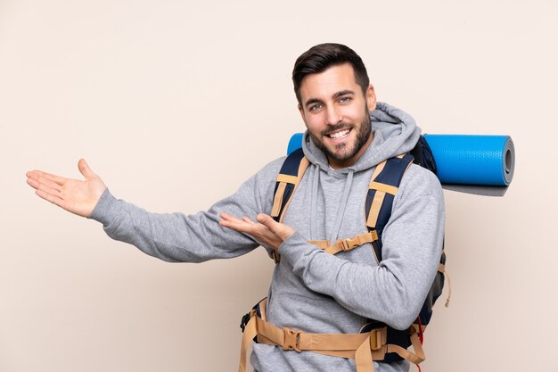 Homem jovem alpinista com uma mochila grande sobre parede isolada, estendendo as mãos para o lado para convidar para vir