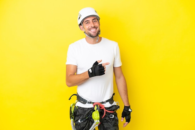 Homem jovem alpinista isolado em fundo amarelo, apontando o dedo para o lado