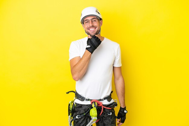 Homem jovem alpinista isolado em fundo amarelo com óculos e sorrindo