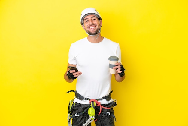 Homem jovem alpinista isolado em fundo amarelo segurando café para levar e um celular