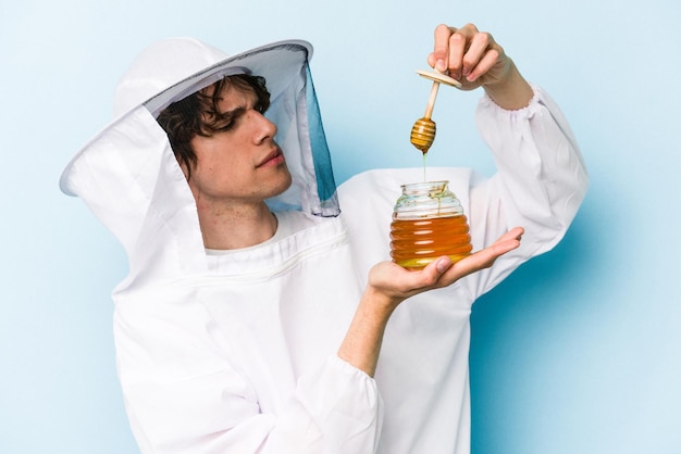 Homem jovem apicultor caucasiano segurando mel isolado em fundo azul