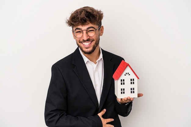 Homem jovem árabe imobiliário segurando uma casa modelo isolada em um fundo isolado, rindo e se divertindo.