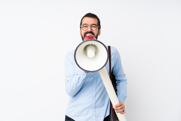 Homem jovem arquiteto com barba sobre parede branca isolada, gritando através de um megafone