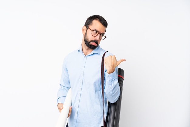 Foto homem jovem arquiteto com barba sobre parede branca isolada infeliz e apontando para o lado