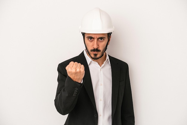 Homem jovem arquiteto usando um capacete de construção isolado no fundo branco, mostrando o punho para a câmera, expressão facial agressiva.