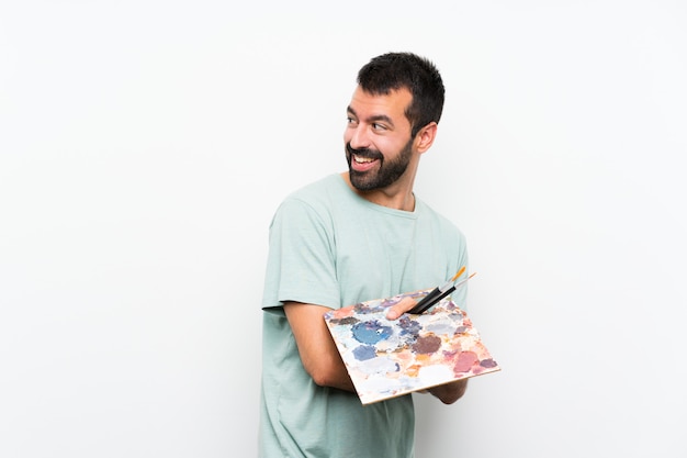 Homem jovem artista segurando uma paleta com os braços cruzados e feliz