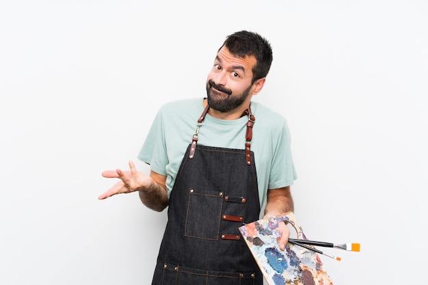 Homem jovem artista segurando uma paleta sobre parede isolada, fazendo o gesto de dúvidas