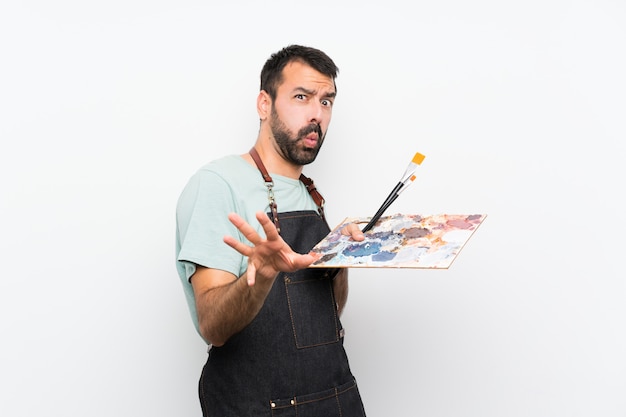 Homem jovem artista segurando uma paleta sobre parede isolada nervosa, esticando as mãos para a frente