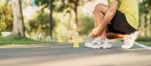 Homem jovem atleta amarrando tênis de corrida com corredor masculino de água Energy Drink pronto para fazer jogging fora da Ásia Fitness andando e exercitando no parque manhã bem-estar bem-estar e conceitos esportivos