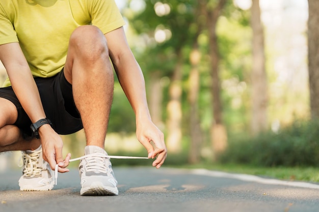 Homem jovem atleta amarrando tênis no corredor masculino ao ar livre do parque pronto para fazer jogging na estrada fora da Ásia Fitness andando e exercitando na trilha em conceitos de bem-estar e esporte matinais