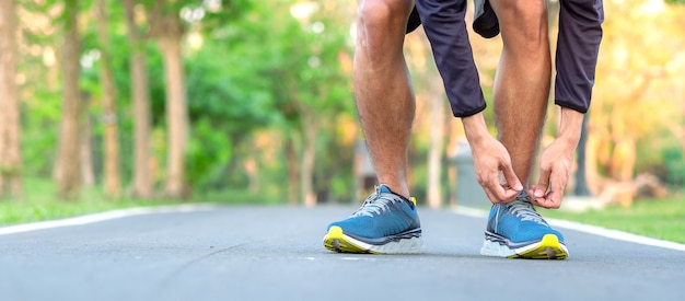 Homem jovem atleta amarrando tênis no parque ao ar livre