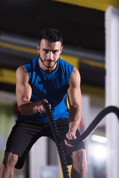 homem jovem atleta apto malhando na academia de treinamento funcional fazendo exercícios de cordas de batalha como parte do treinamento de fitness cruzado