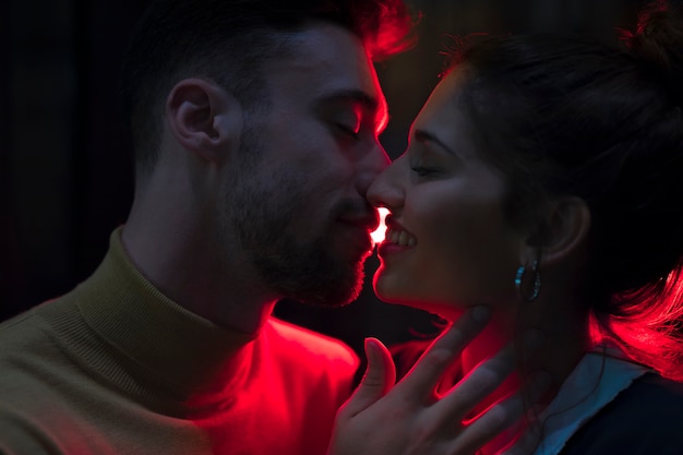 Foto homem jovem, beijando, mulher sorridente, iluminado, por, luzes vermelhas