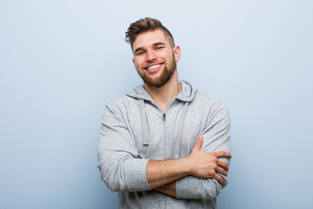 Homem jovem bonito fitness que se sente confiante, cruzando os braços com determinação.