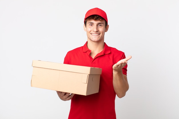 Homem jovem bonito sorrindo alegremente com simpáticos e oferecendo e mostrando um conceito de serviço de pacote de entrega de conceito.