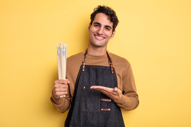 Homem jovem bonito sorrindo alegremente, sentindo-se feliz e mostrando um conceito. conceito de artista