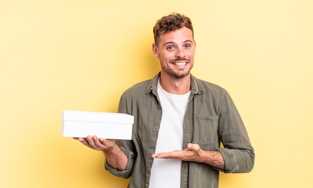 Homem jovem bonito sorrindo alegremente, sentindo-se feliz e mostrando um conceito. conceito de caixa branca