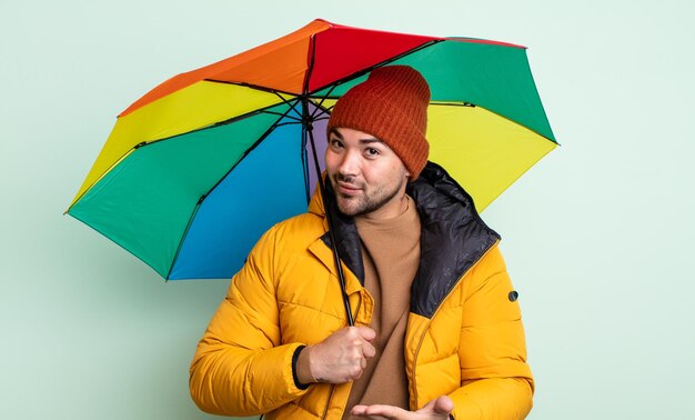 Homem jovem bonito sorrindo alegremente, sentindo-se feliz e mostrando um conceito. conceito de chuva e guarda-chuva