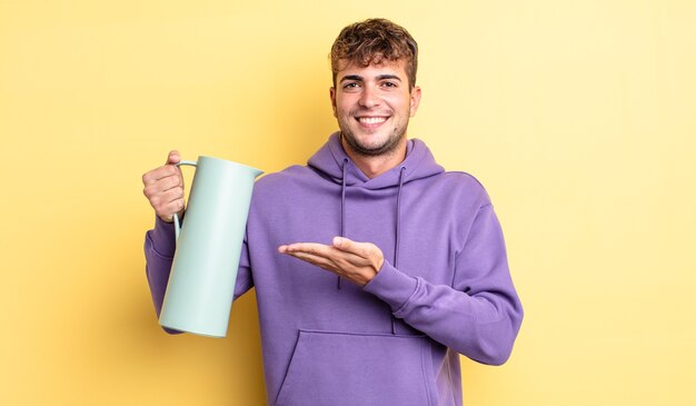 Homem jovem bonito sorrindo alegremente, sentindo-se feliz e mostrando um conceito. conceito de garrafa térmica