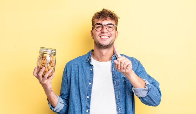 Homem jovem bonito sorrindo com orgulho e com confiança, fazendo o número um. conceito de garrafa de biscoitos