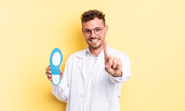 Homem jovem bonito sorrindo com orgulho e com confiança, fazendo o número um. conceito de quiropodista