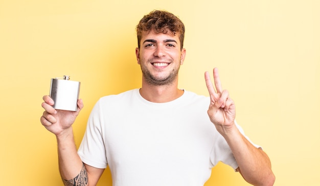 Homem jovem bonito sorrindo e parecendo amigável, mostrando o número dois. conceito de frasco de álcool