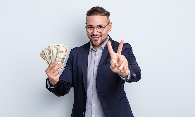 Homem jovem bonito sorrindo e parecendo amigável, mostrando o número dois. conceito de notas de dólar